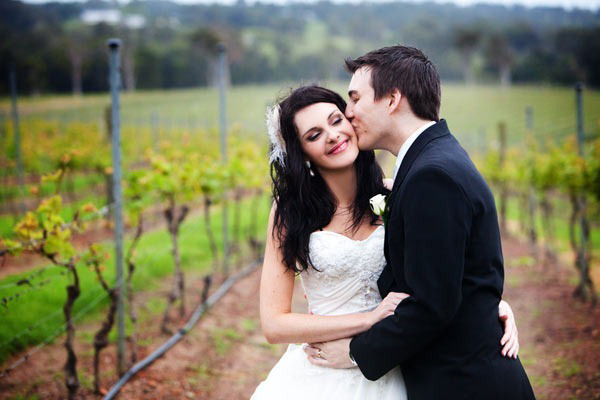 groom kissing bride in vineyard