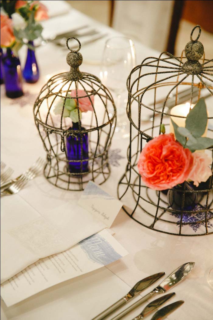 Dining table centrepiece arranged in birdcage and blue bottle